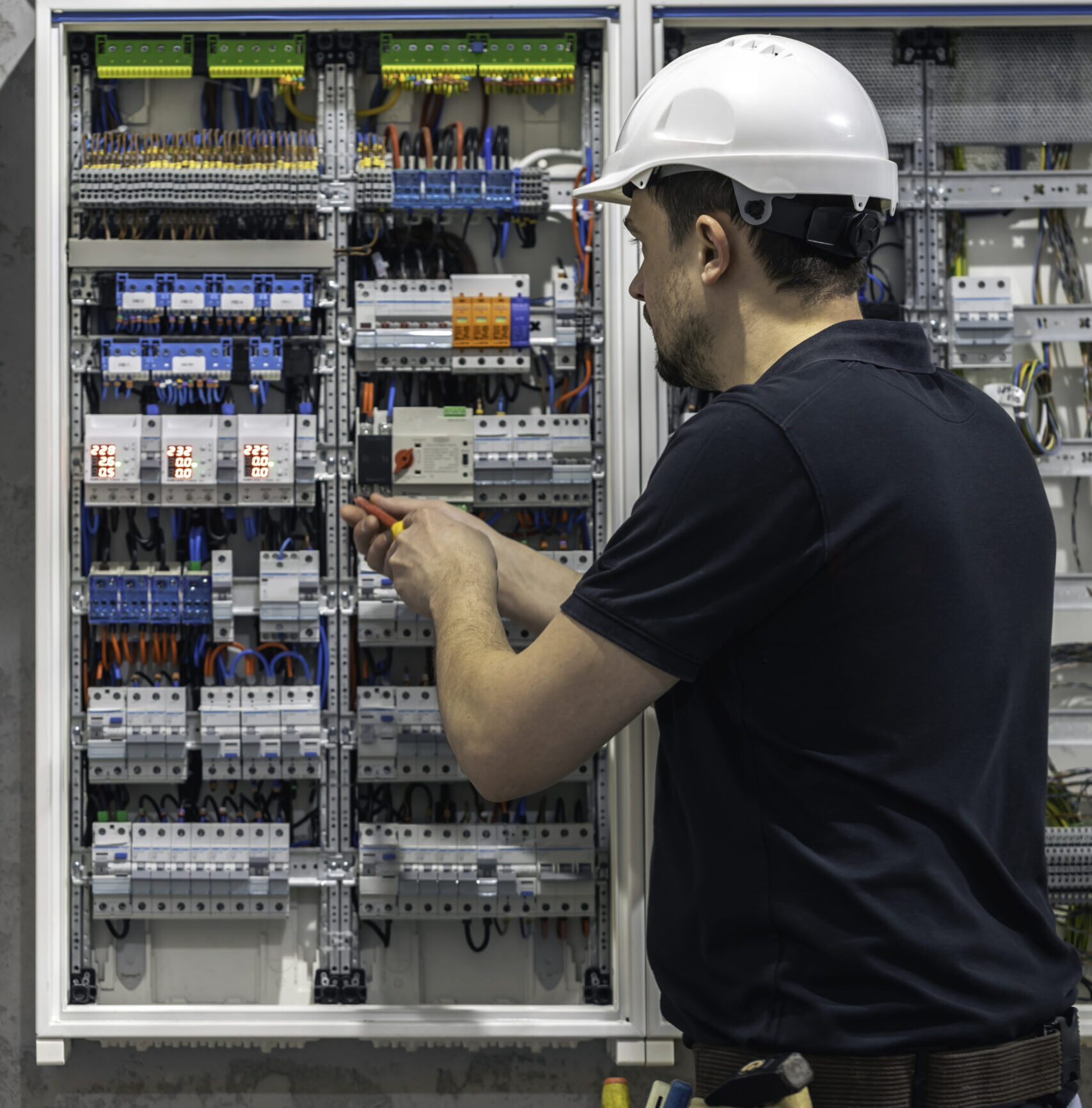 a male electrician works in a switchboard using an electrical connection cable.